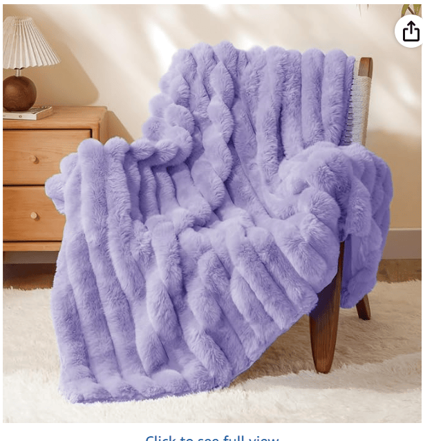 A soft, plush lavender blanket draped over a wooden chair, with a bedside table and a decorative lamp in the background.